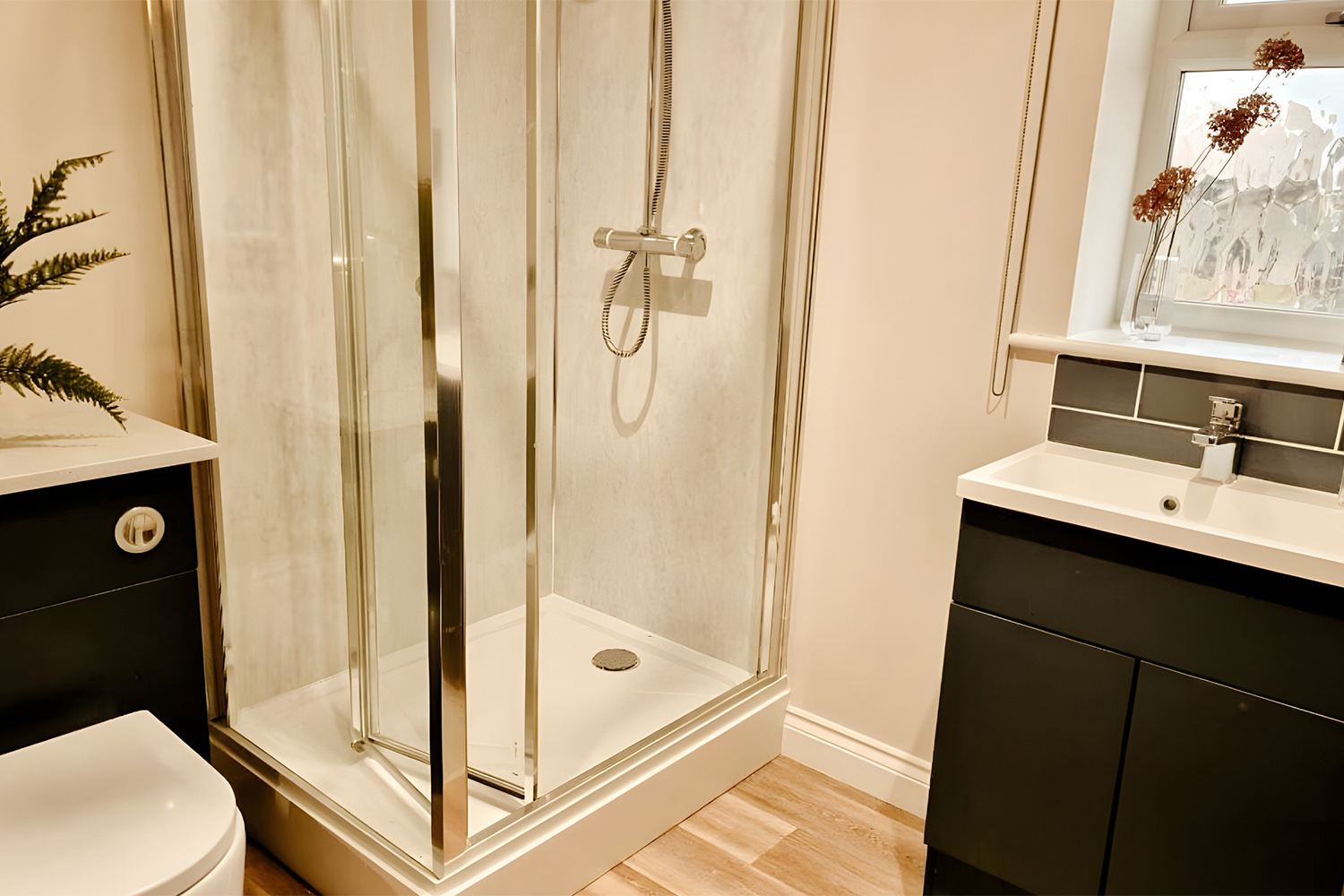 Modern bathroom with a glass shower enclosure, sleek black vanity units and natural wood-effect flooring, styled in a warm, contemporary finish.