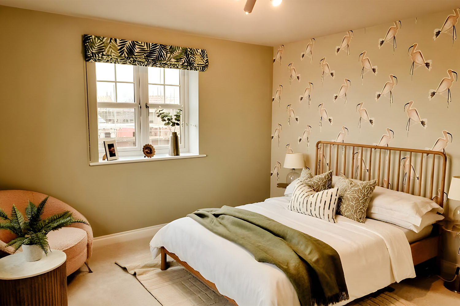 A bright double bedroom with soft green tones, flamingo feature wallpaper and warm layered textiles, offering a comfortable and uplifting feel.