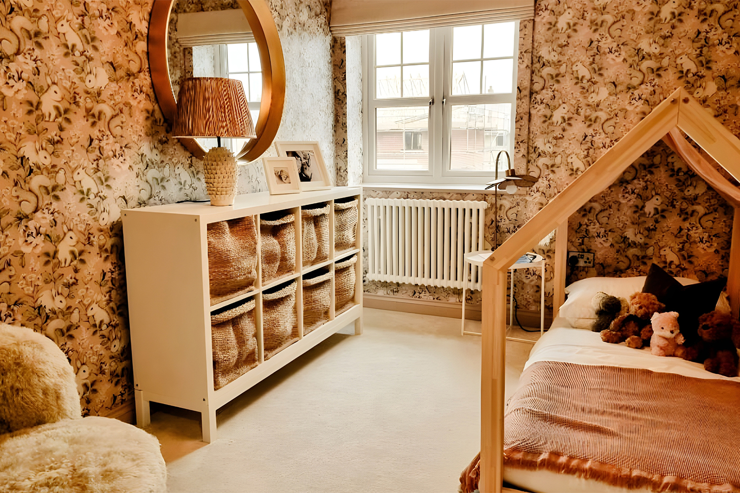 A playful children’s bedroom with patterned woodland wallpaper, a low house-frame bed and woven storage baskets, designed to feel warm and imaginative.