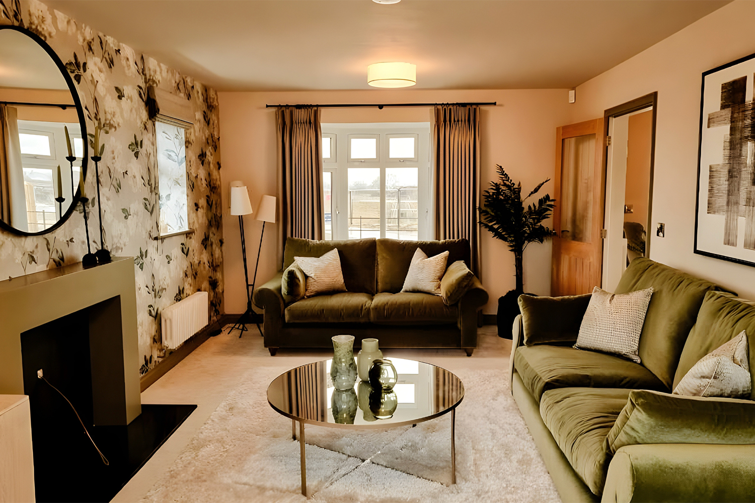 A spacious family lounge with green velvet sofas, floral feature wallpaper and large windows, styled for comfort and modern everyday living.