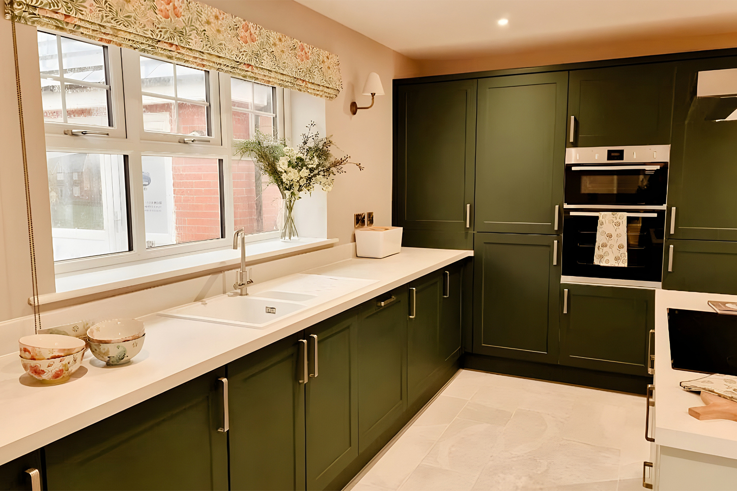 Modern kitchen with deep green cabinets, white worktops and floral window dressing, offering a stylish and contemporary cooking space.