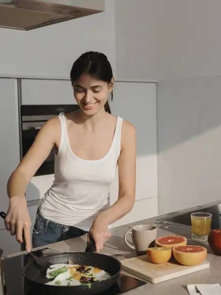 Woman cooking eggs in a bright modern kitchen, smiling while using a frying pan.