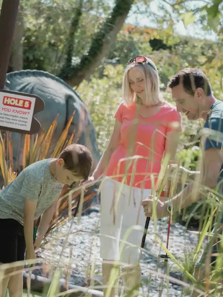 Family playing mini golf together outdoors on a sunny day.