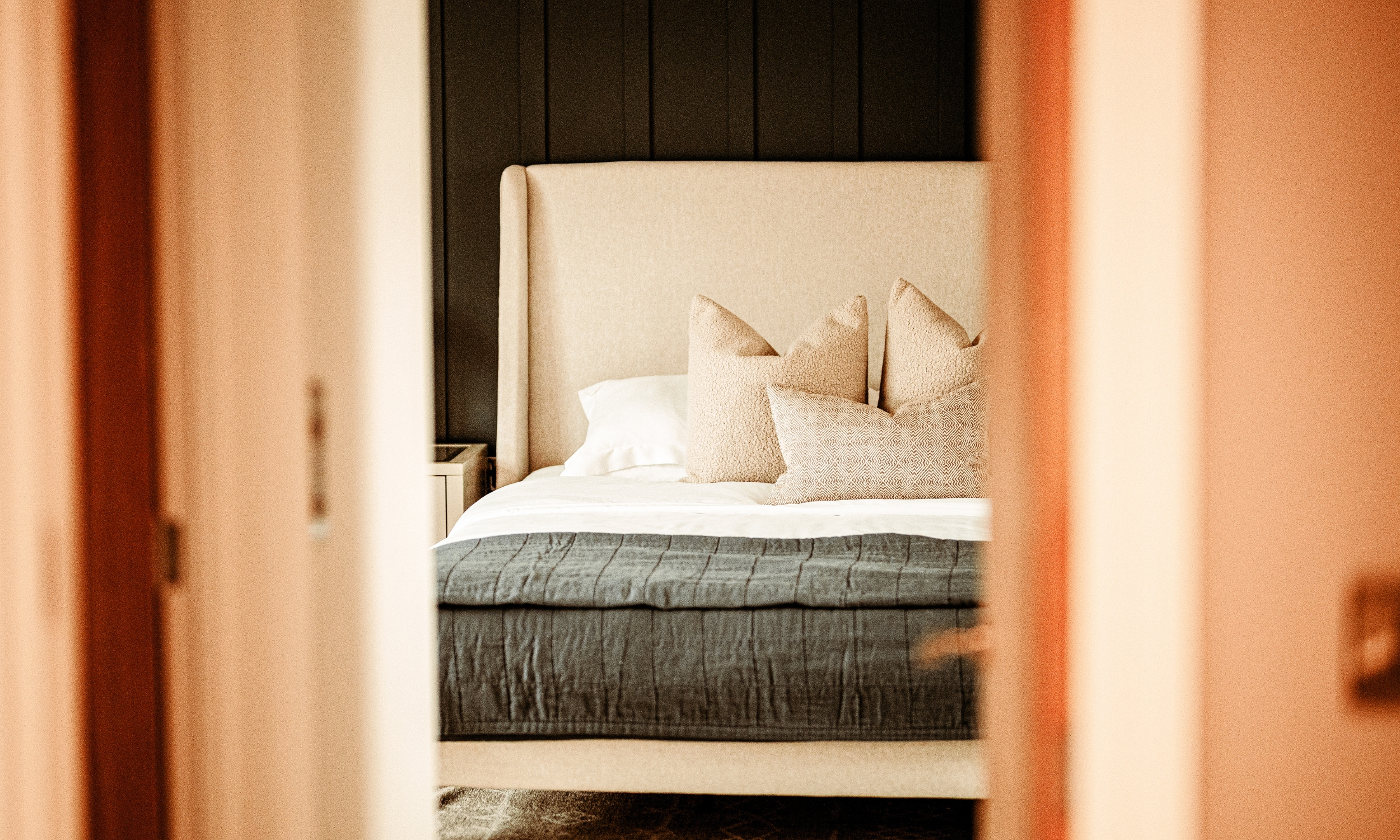 Spacious master bedroom with neutral furnishings, a deep-panelled feature wall, and large windows filling the room with light - a refined retreat in a Broadgate home.