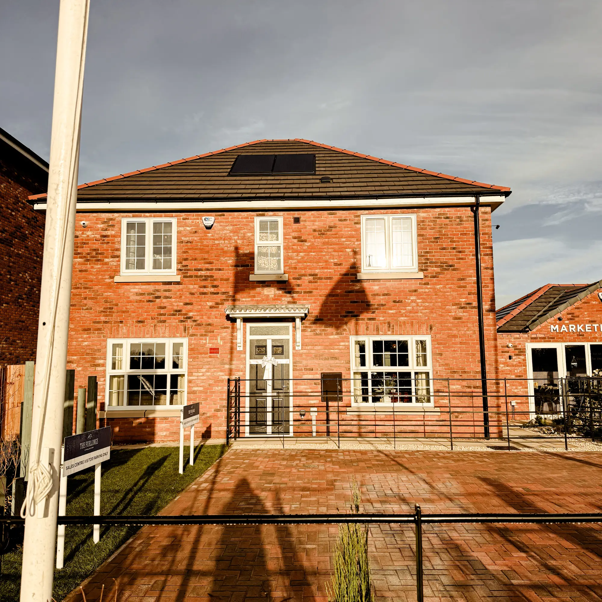 Front exterior of a red-brick Broadgate Show Home at The Furlongs, featuring solar panels on the roof and landscaped paving leading to the front door.