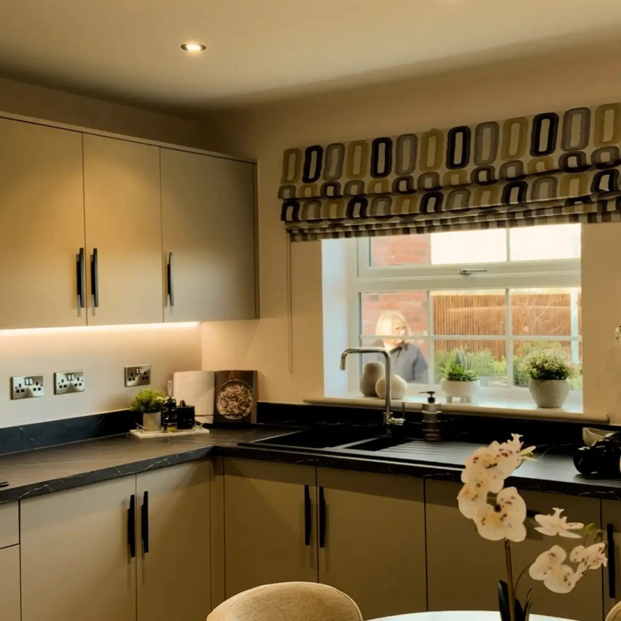 Modern kitchen interior with soft neutral cabinetry, under-cabinet lighting, plants on the windowsill and contemporary worktops.