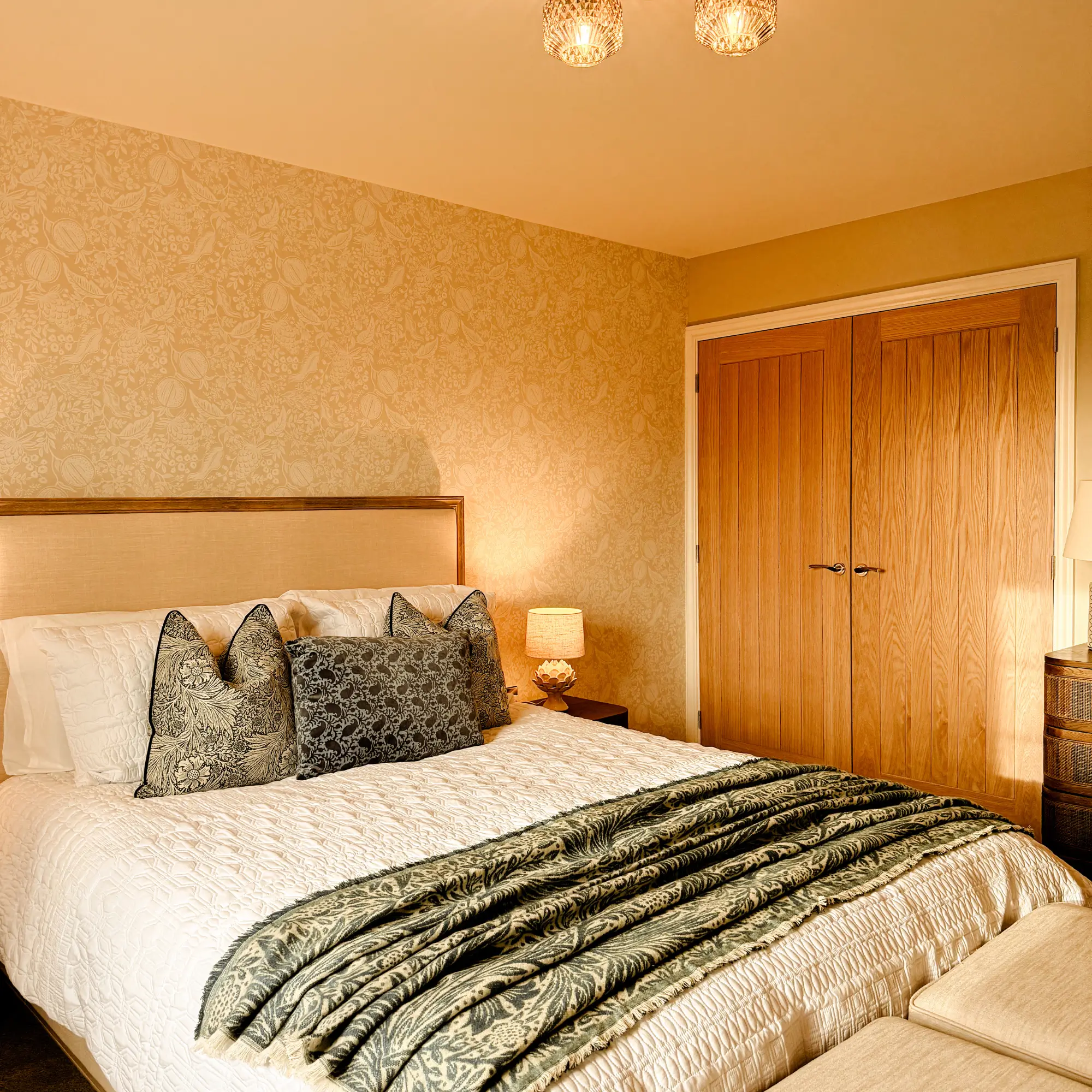 Cosy children’s bedroom with hot-air-balloon wallpaper, a wooden spindle bed, soft toys arranged at the pillow, and a window bringing in natural light.
