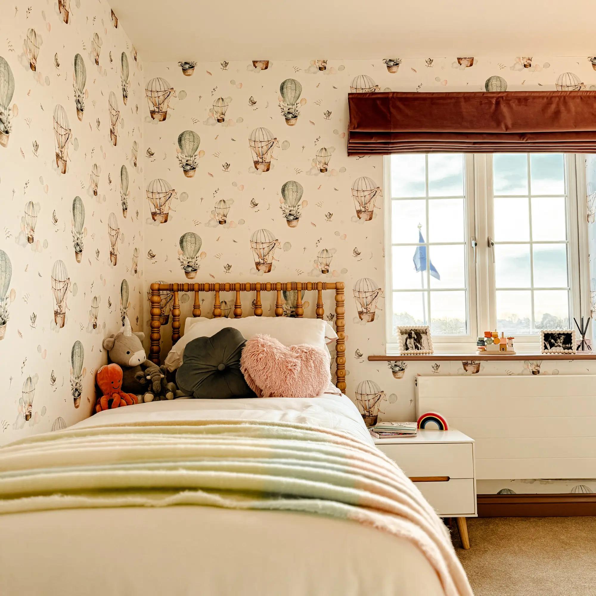Primary bedroom with warm botanical wallpaper, a neatly dressed bed with textured cushions and a patterned throw, wooden double wardrobe doors and soft ambient lighting.