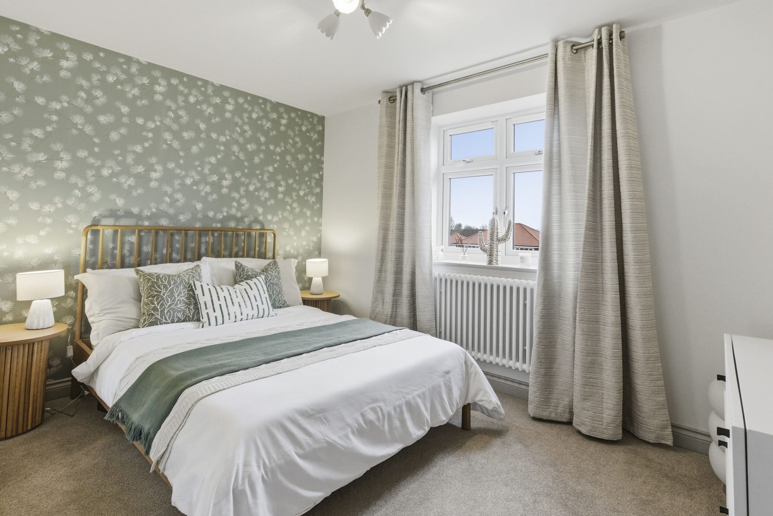 Modern bedroom with green patterned feature wall, wooden bed frame, neutral bedding, and large window creating a calm and welcoming space.