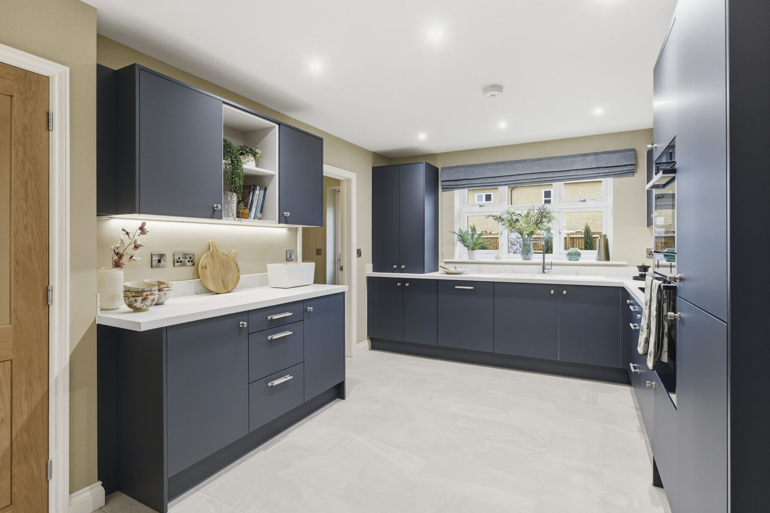 Contemporary kitchen interior with deep blue cabinetry, white quartz worktops, integrated appliances, and under-cabinet lighting in a new Broadgate Homes property.