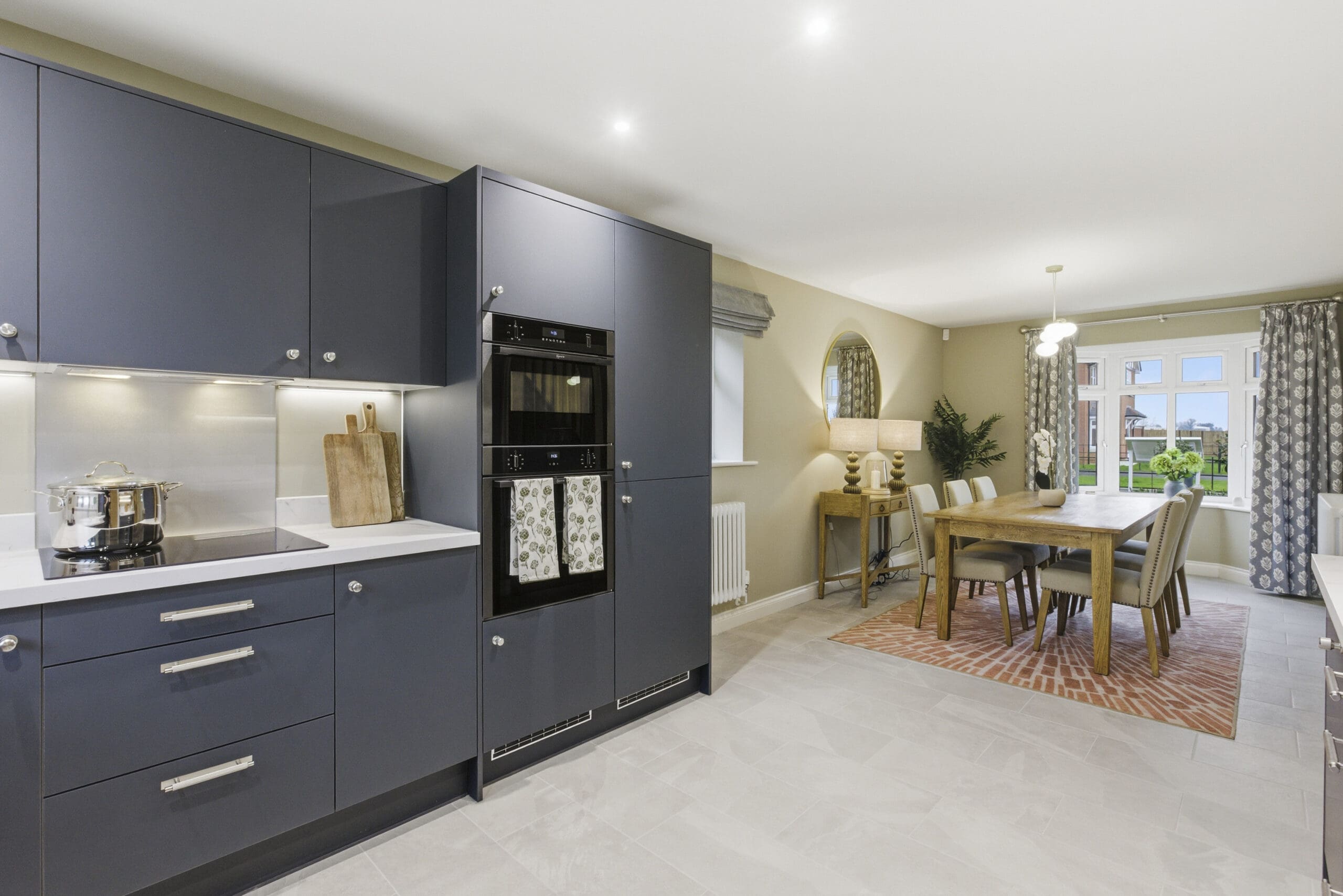Contemporary kitchen interior with deep blue cabinetry, white quartz worktops, integrated appliances, and under-cabinet lighting in a new Broadgate Homes property.