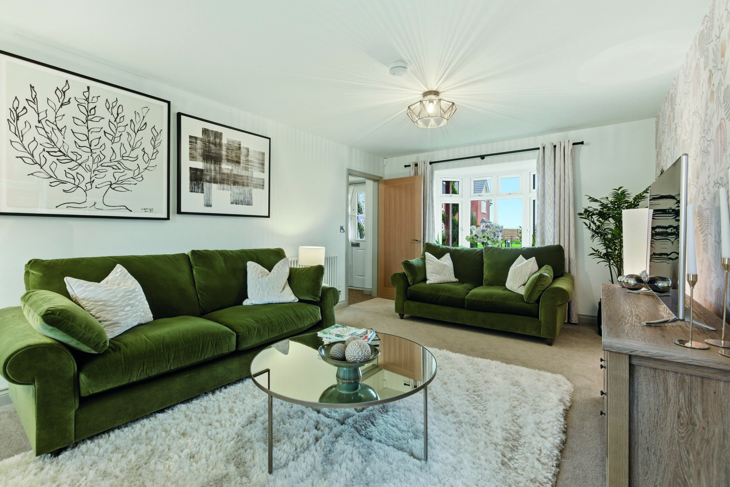 Living room at Gleneagles Drive, Woodhall Spa, with two green velvet sofas, a round mirrored coffee table, and botanical framed artwork.
