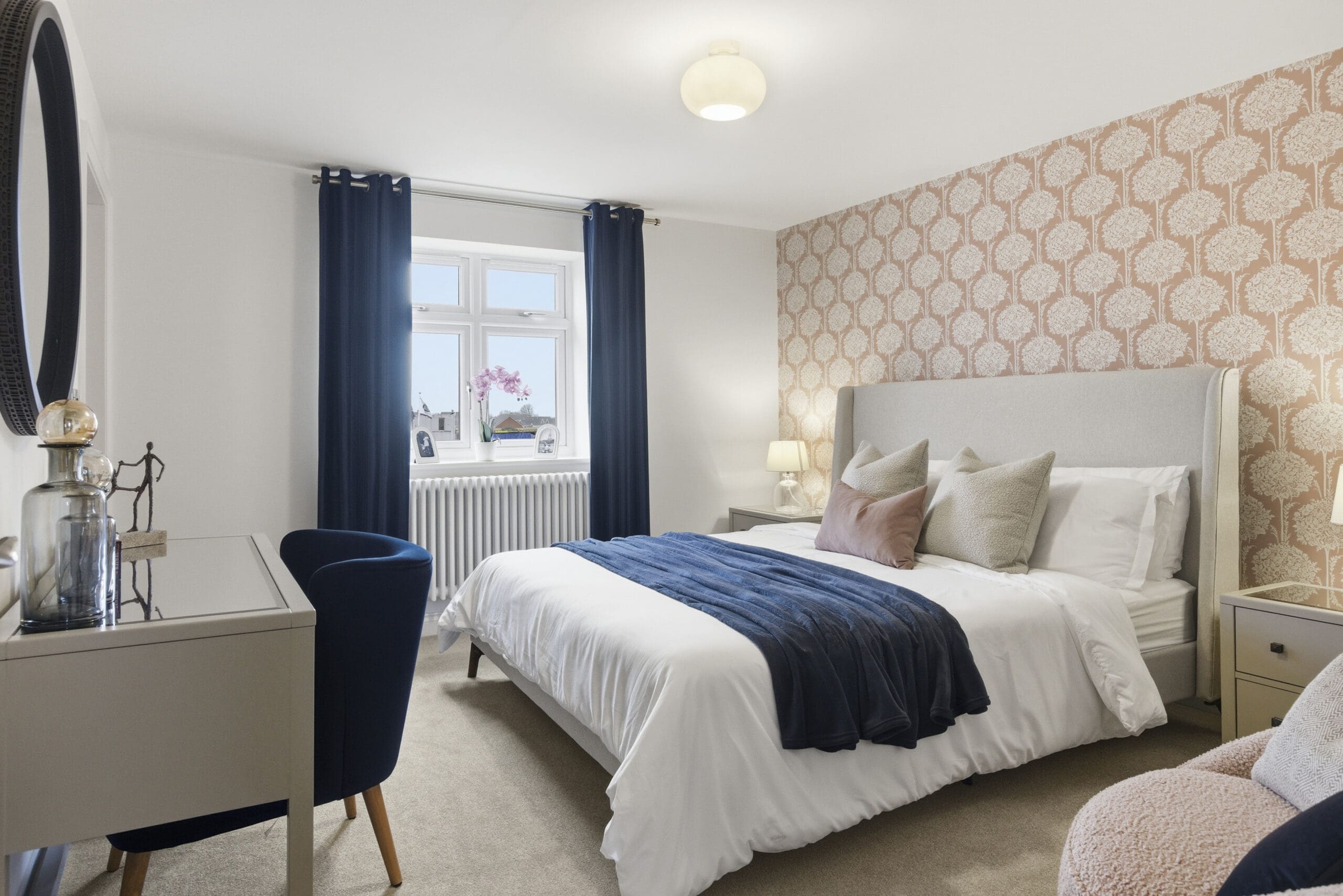 Bedroom at Gleneagles Drive, Woodhall Spa, with blush floral feature wallpaper, navy curtains, and a dressing table with round mirror.