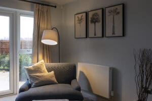 Cosy lounge with a comfortable armchair, floor lamp, neutral décor and large patio doors overlooking the garden at The Furlongs at Holland Park.