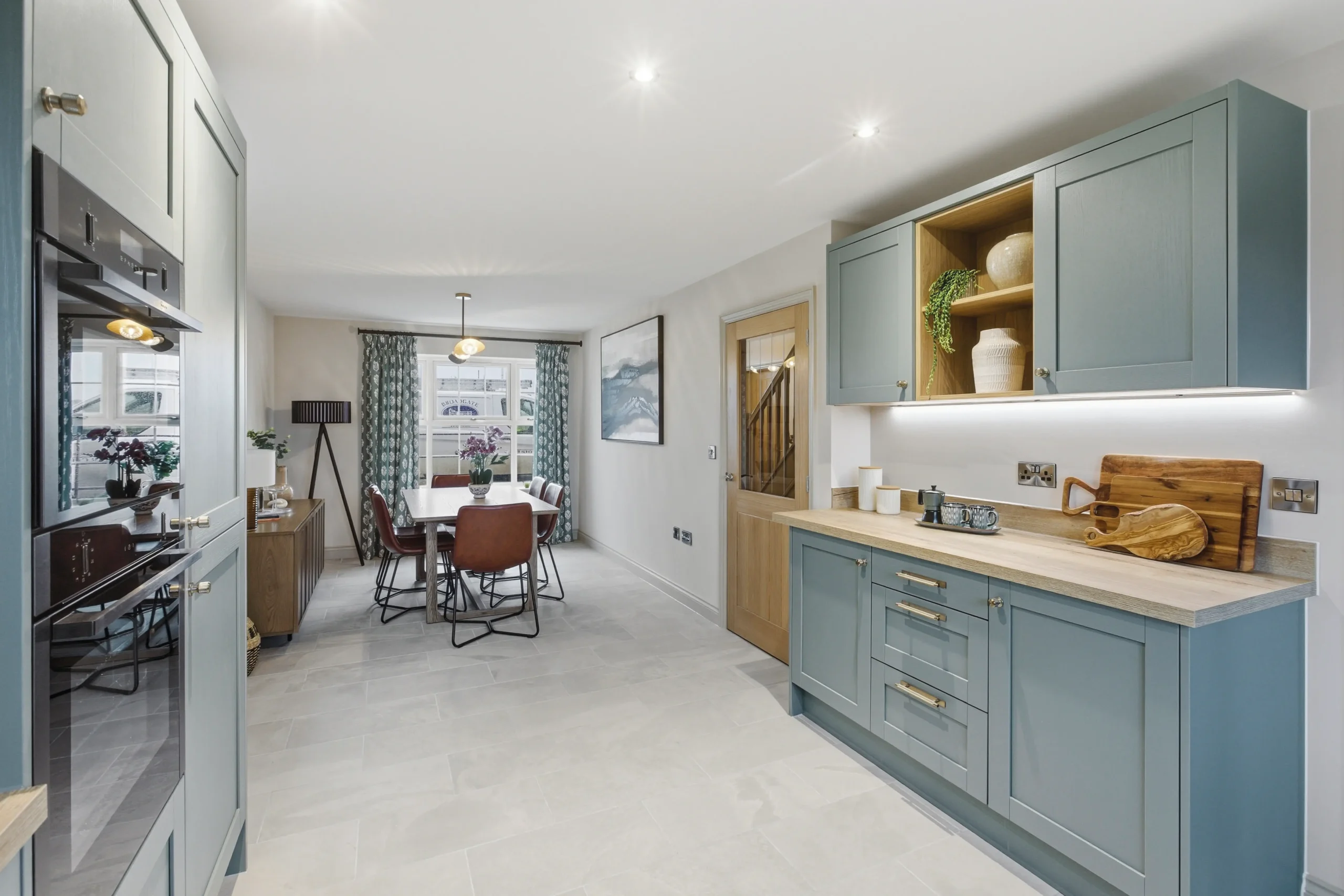 Open-plan kitchen and dining area at The Furlongs, Holland Park, Spalding, featuring sage green shaker-style cabinetry and a dining table with burgundy leather chairs.