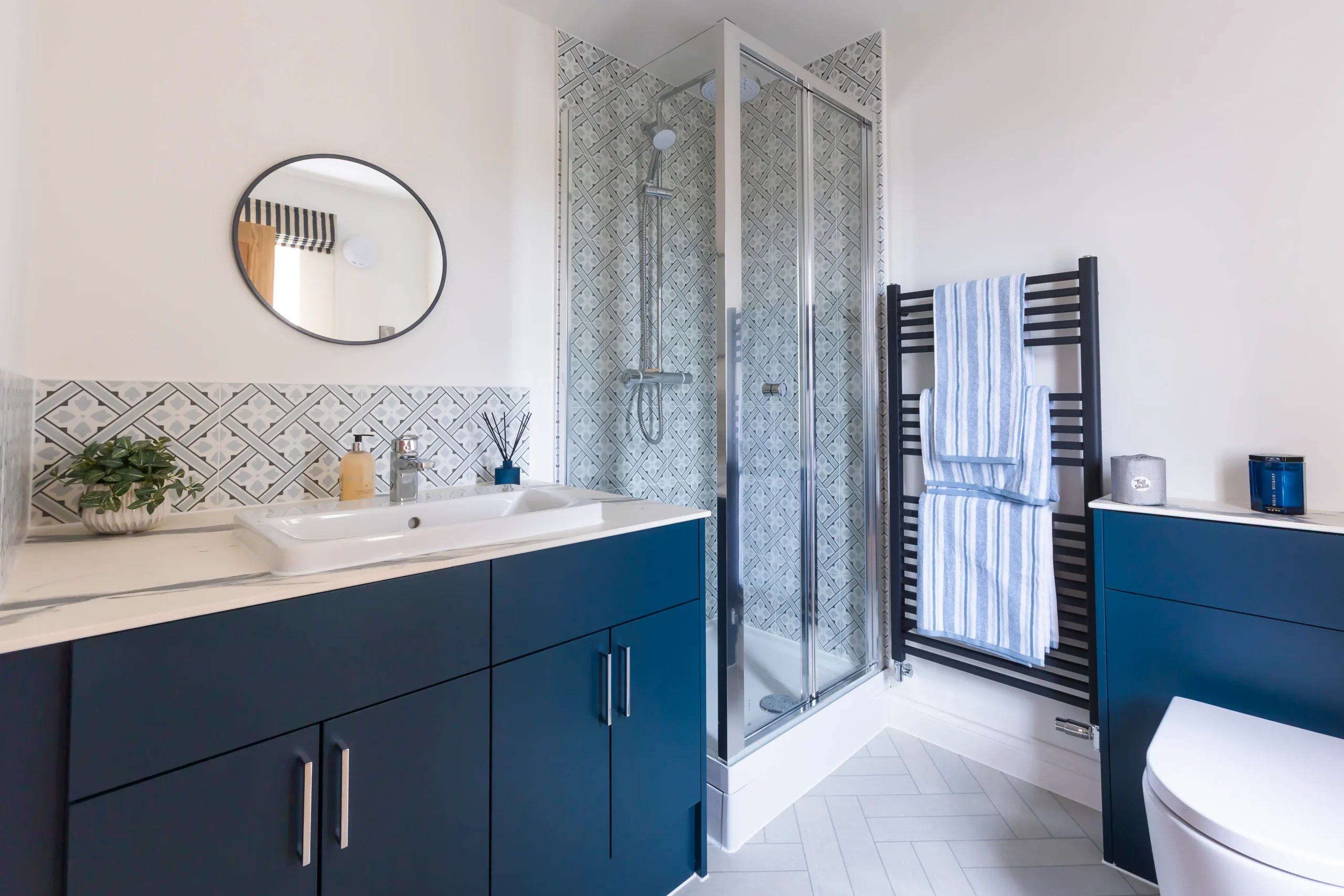 En-suite bathroom at The Furlongs, Holland Park, Spalding, with navy vanity unit, patterned tiled splashback, and black ladder-style heated towel rail.