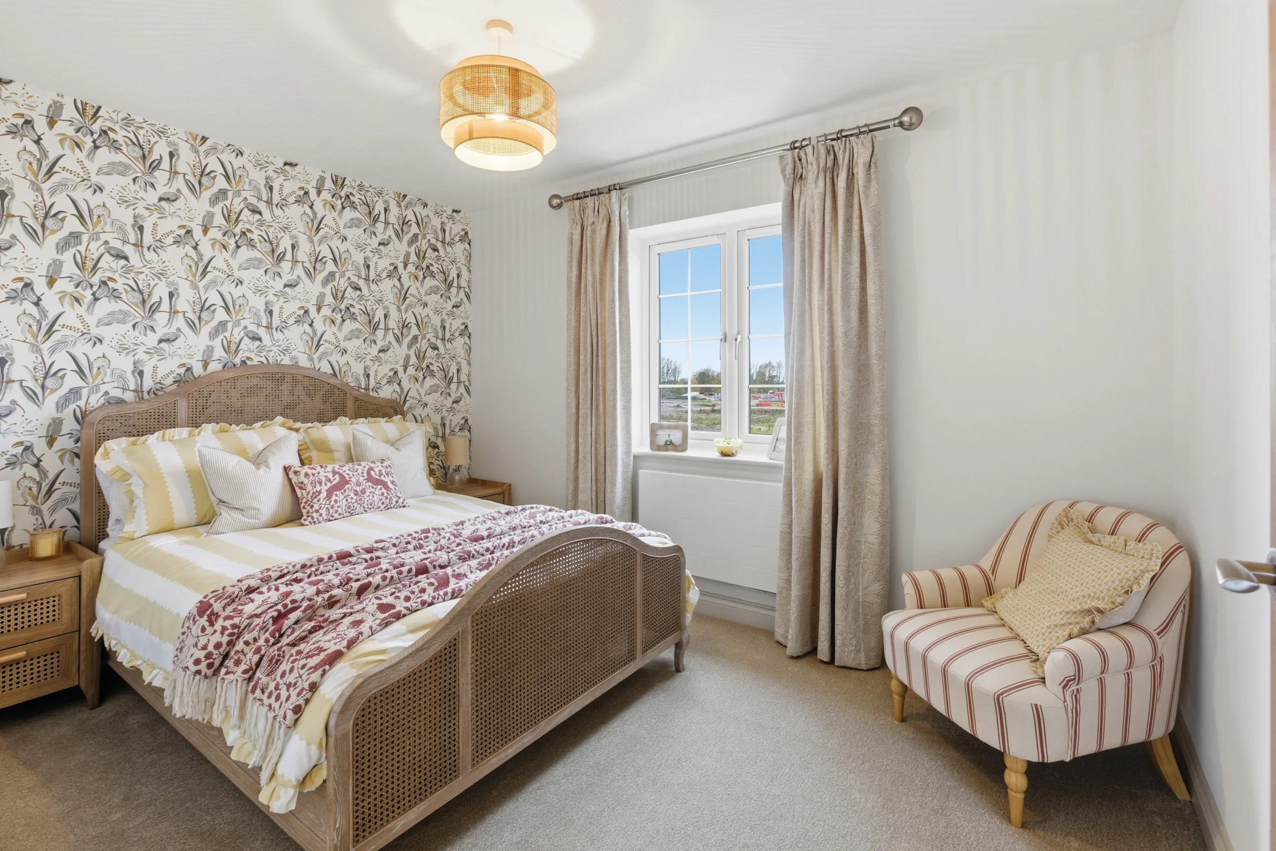 Second bedroom at The Furlongs, Holland Park, Spalding, with botanical print feature wallpaper, rattan-detail bed frame, and striped upholstered armchair.