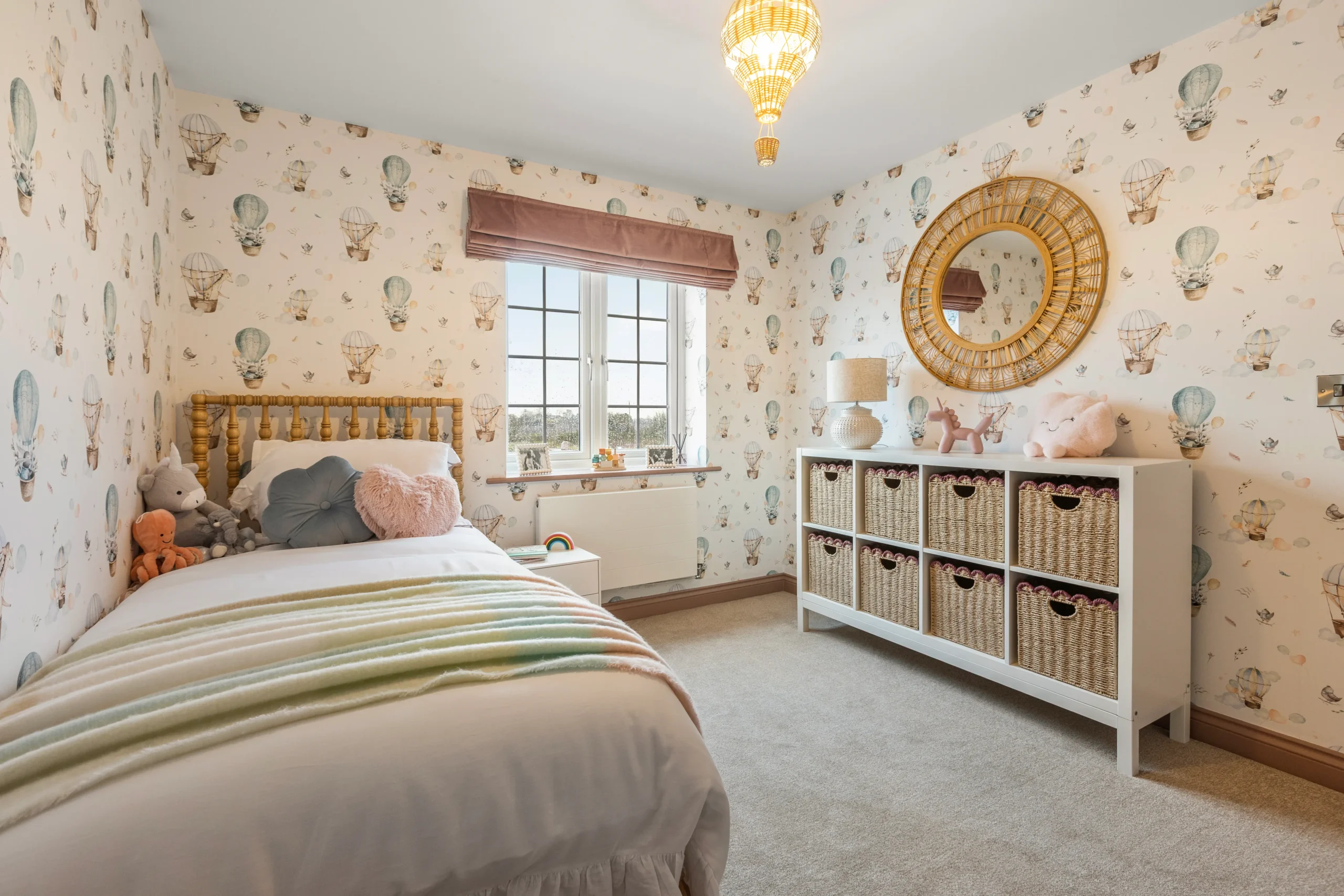 Children's bedroom at The Furlongs, Holland Park, Spalding, with hot air balloon print wallpaper, rattan mirror, and woven storage baskets.