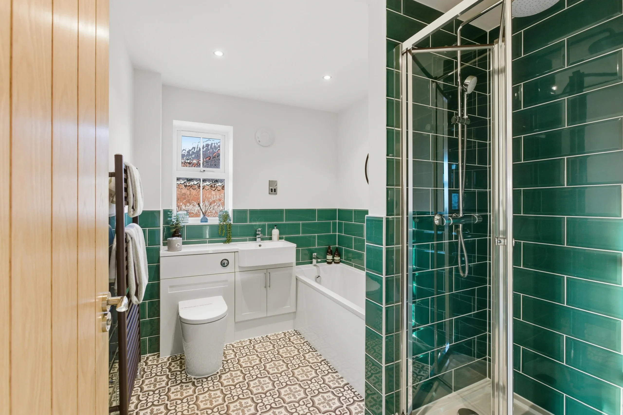 Family bathroom at The Furlongs, Holland Park, Spalding, with forest green metro tiles, patterned floor tiles, and separate bath and shower.