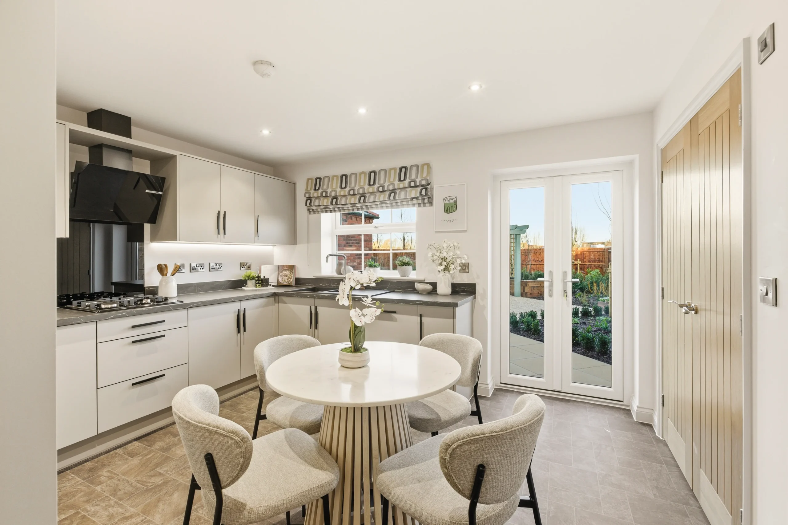 Kitchen diner at The Furlongs, Holland Park, Spalding, with pale grey cabinetry, dark stone worktops, and French doors opening onto the garden.