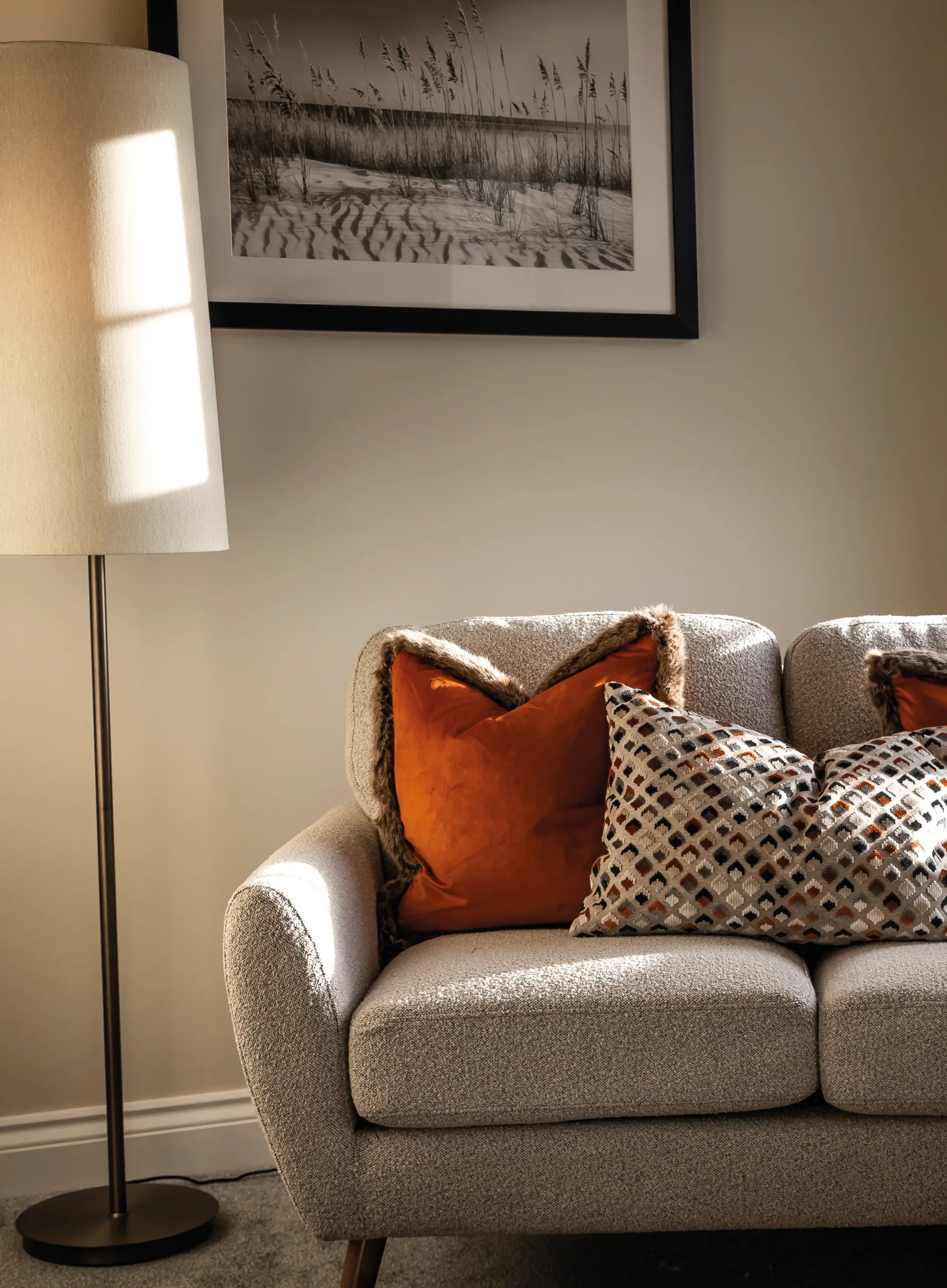 Lounge seating detail at The Furlongs, Holland Park, Spalding, with grey boucle sofa, burnt orange and patterned cushions, and framed coastal artwork.