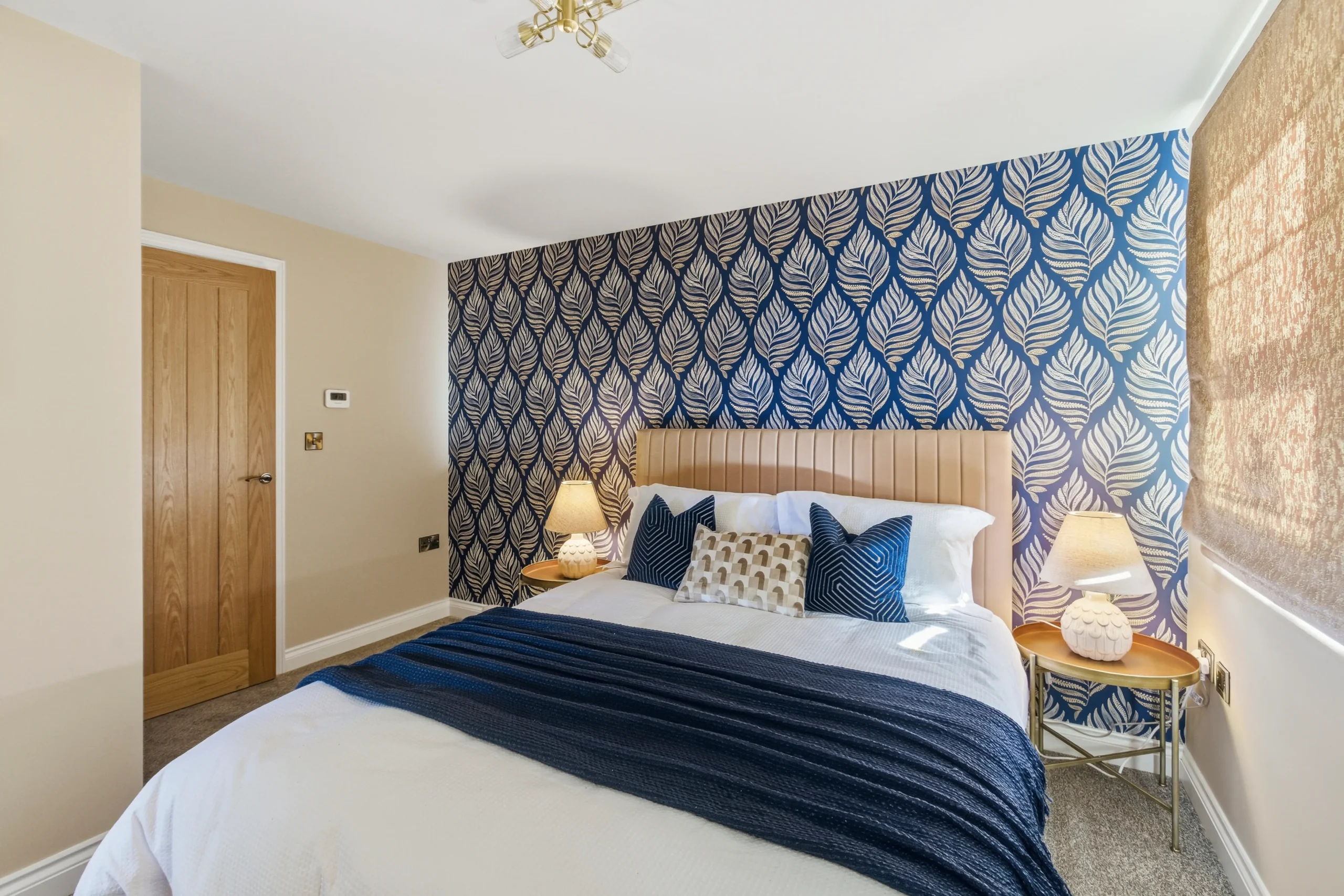 Master bedroom in the 3-bed showhome at The Furlongs, Holland Park, Spalding, with navy leaf-print feature wallpaper and channel-detail headboard.