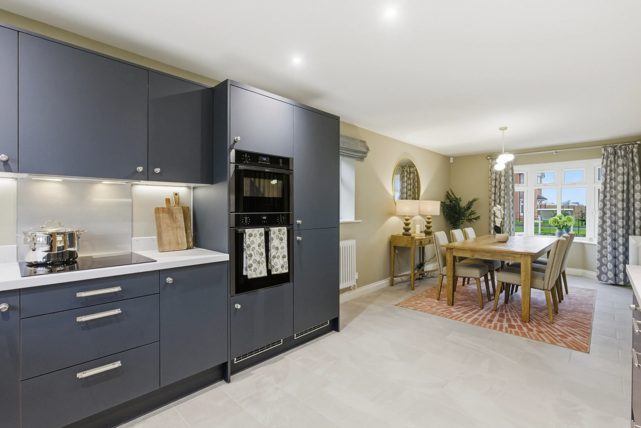 Open-plan kitchen and dining area at Gleneagles Drive, Woodhall Spa, with navy shaker-style cabinetry and a dining table seating six by a bay window.
